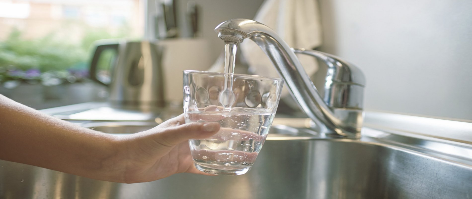 eine Hand hält ein Glas unter den laufenden Wasserhahn